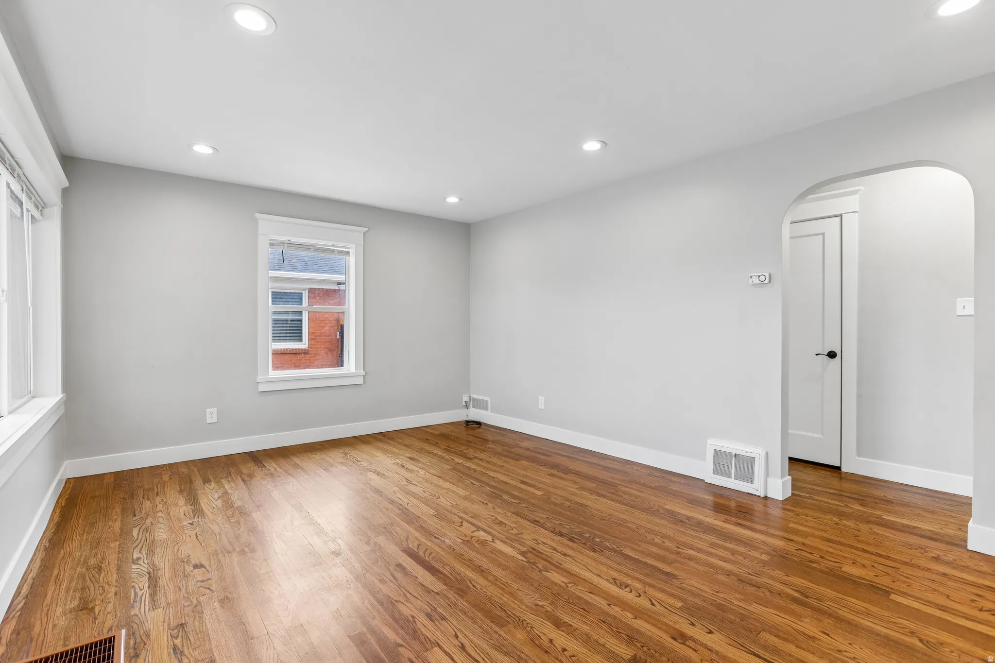 Hardwood flooring, recessed lighting, multiple windows, an arched doorway, and a white paneled door