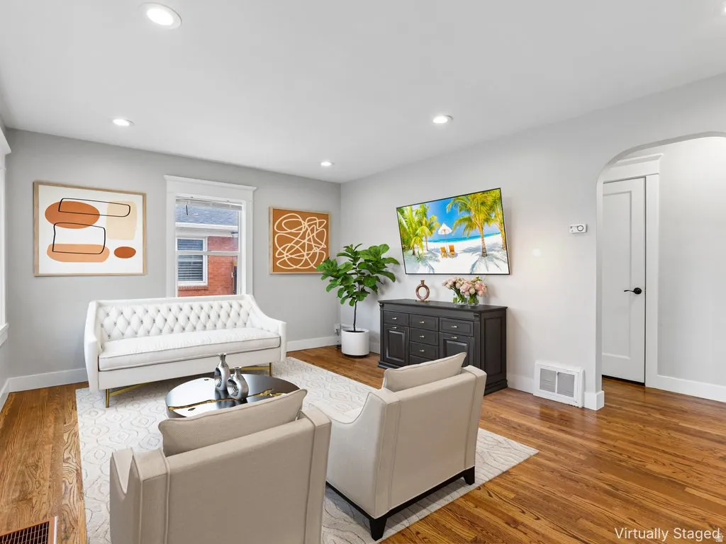 Hardwood flooring, recessed ceiling lighting, arched doorway, white trim, and a built-in wall vent