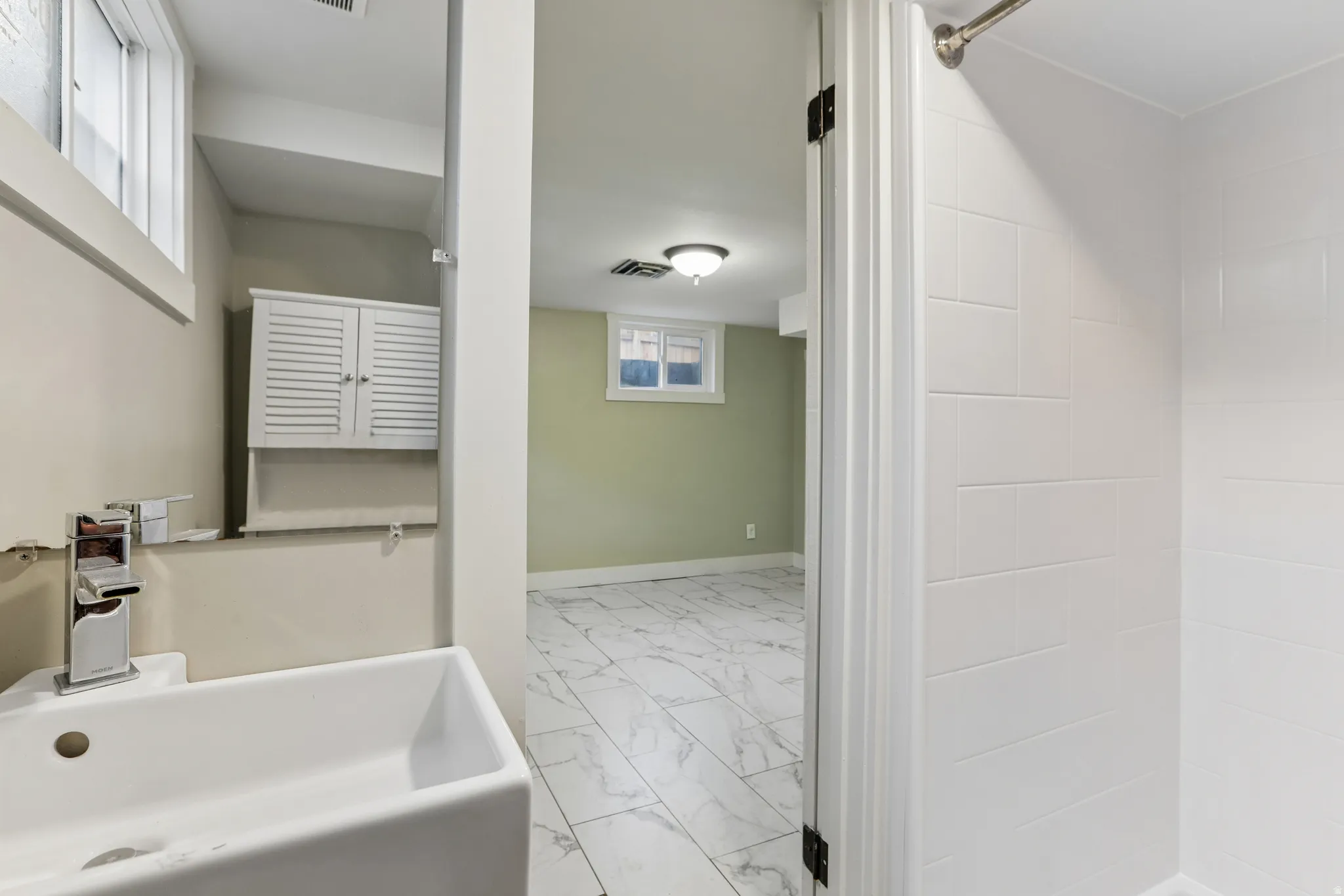 Bathroom featuring a white rectangular vessel sink, chrome faucet, white louvered wall cabinet, and a tiled shower