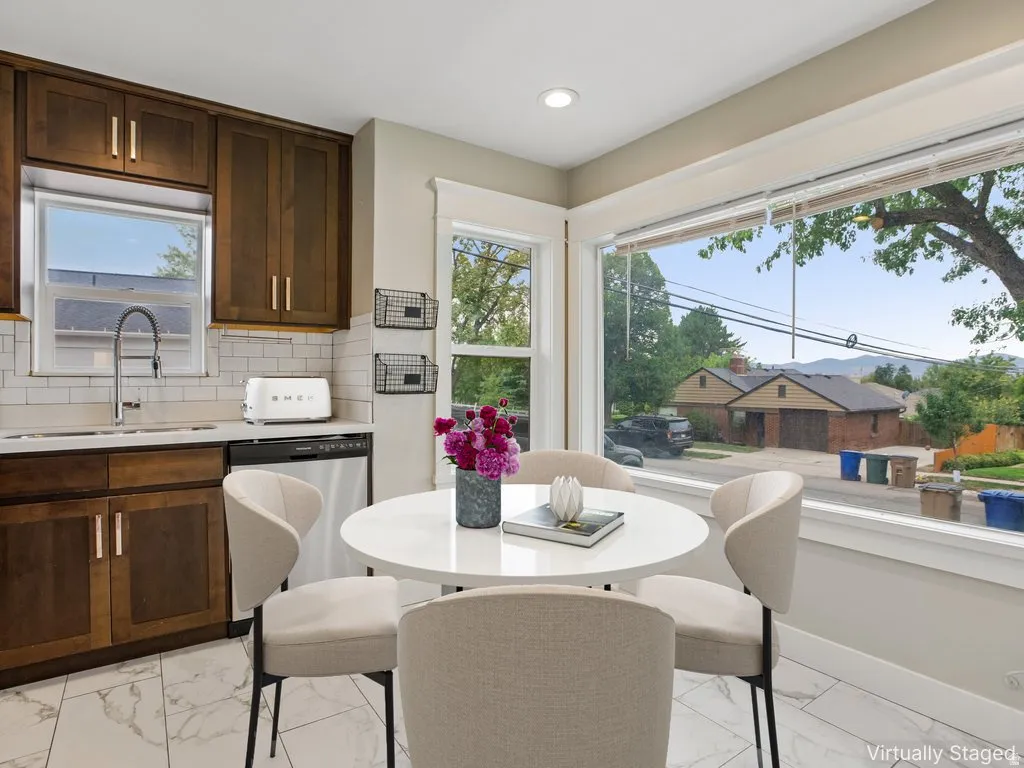 Kitchen featuring white subway tile backsplash, dark wood cabinetry with modern hardware, stainless steel dishwasher, and a large window overlooking natural scenery