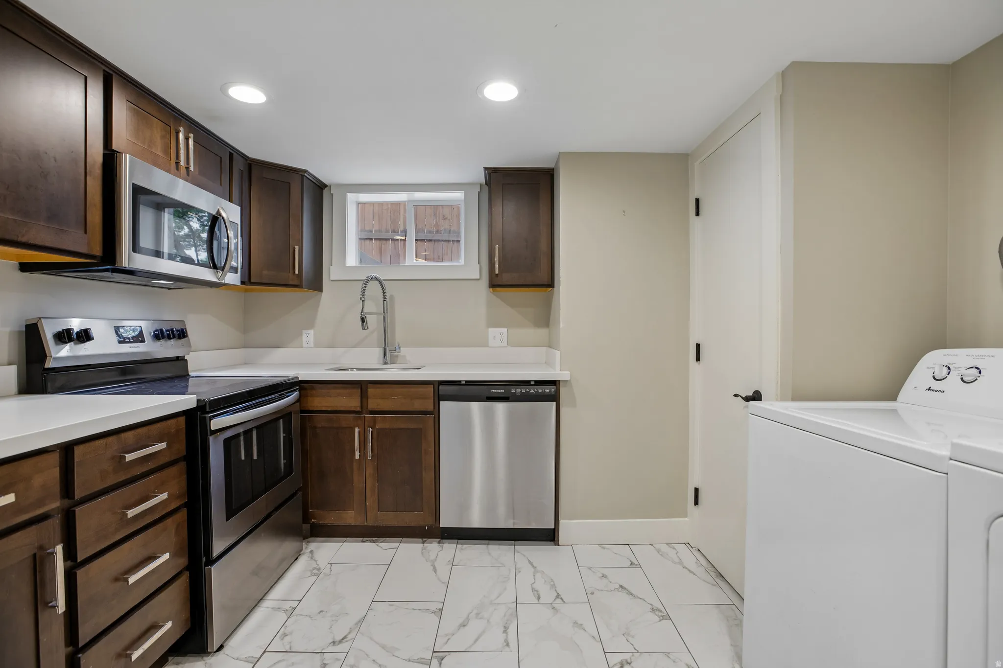 Kitchen featuring wood cabinetry, stainless steel appliances, white countertops, a single basin sink with a gooseneck faucet, and tile flooring
