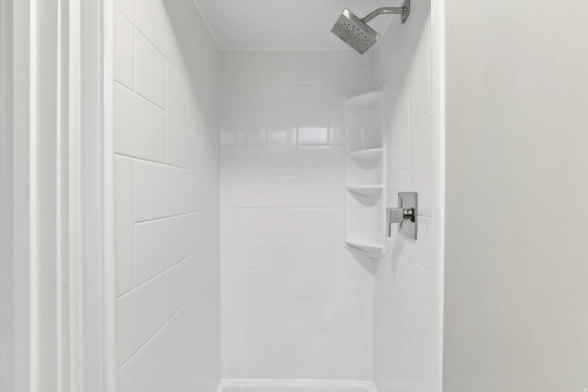 Shower enclosure featuring white subway tile, a chrome rain shower head, and integrated shelving