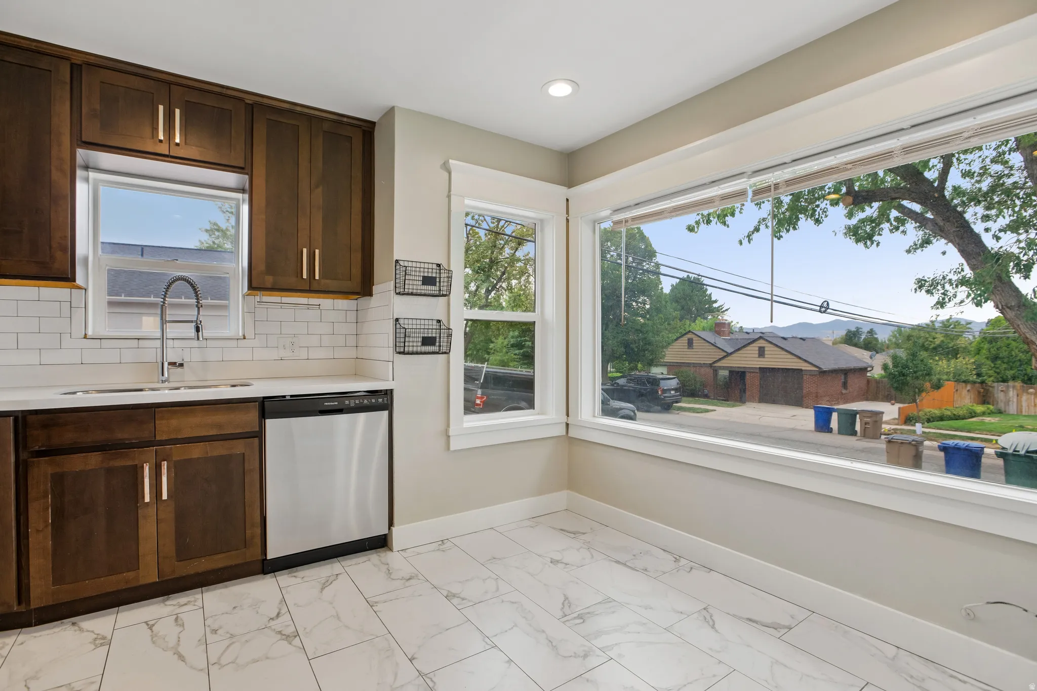 Kitchen featuring wood cabinetry, white subway tile backsplash, a stainless steel dishwasher, and a large window overlooking the exterior