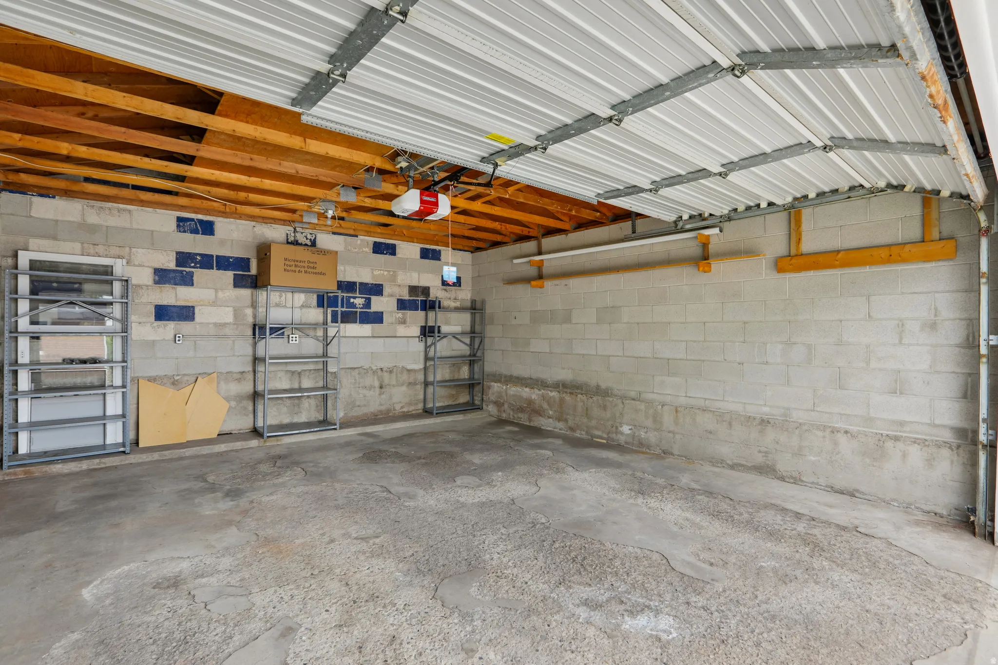 Attached garage with concrete block walls, exposed wood ceiling beams, and a corrugated metal ceiling