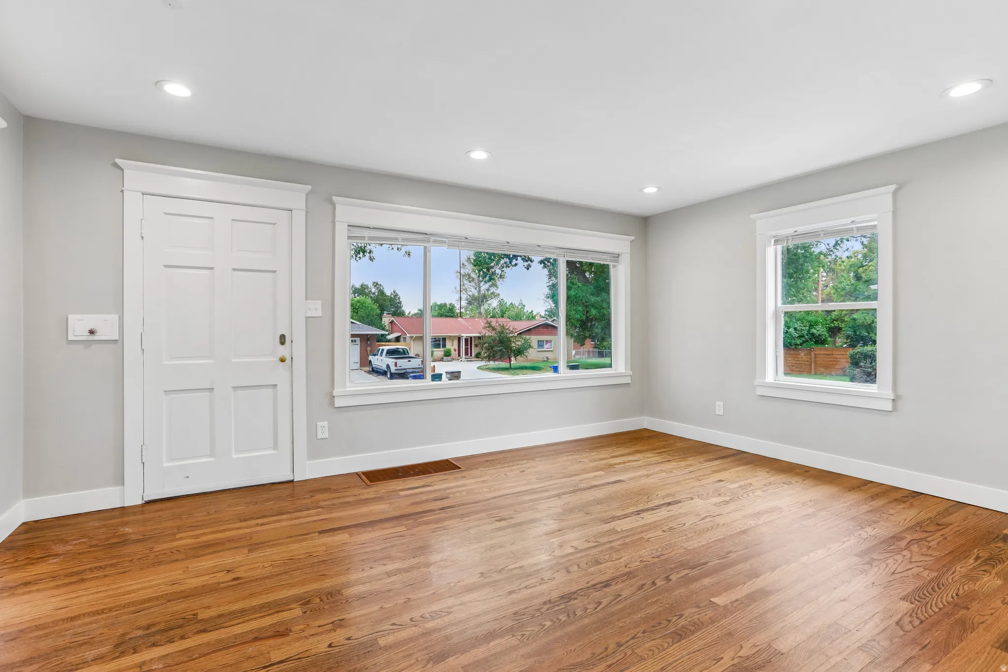 Hardwood flooring, recessed lighting, white trim, multiple windows, and a paneled entry door