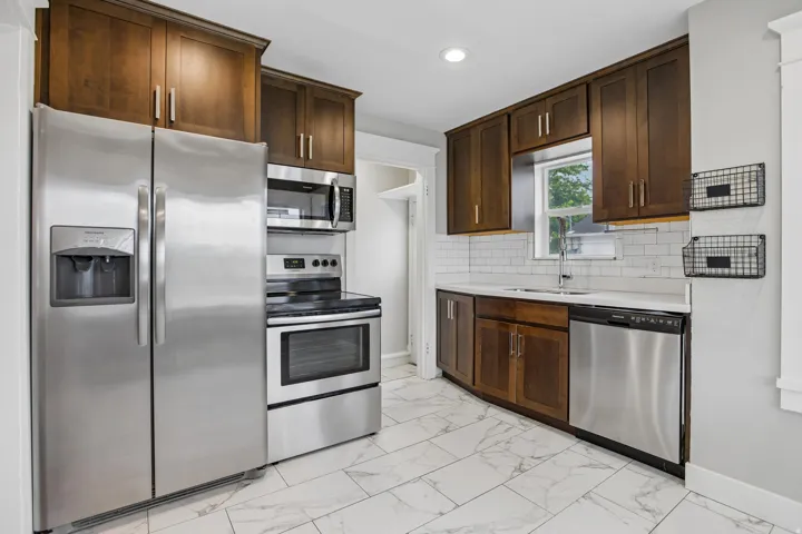 Dark wood-finish cabinetry, stainless steel appliances, white subway tile backsplash, white countertop, and patterned floor tiling