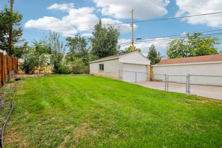 Expansive lawn area with a wood fence, concrete driveway, and a detached two-car garage
