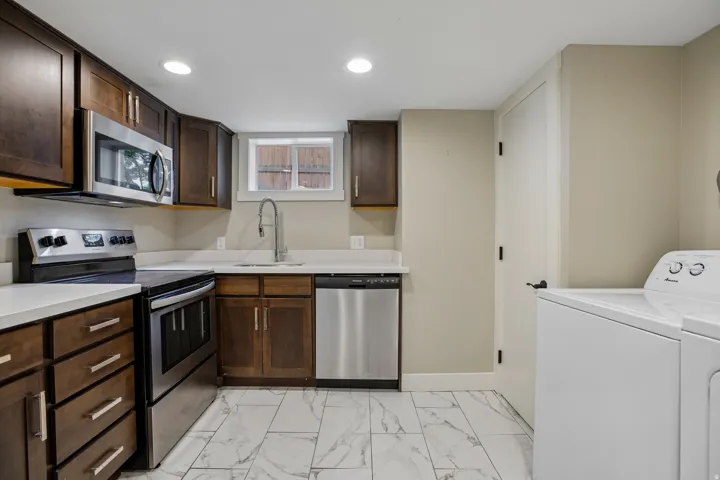 Kitchen featuring wood cabinetry, stainless steel appliances, white countertops, a single basin sink with a gooseneck faucet, and tile flooring