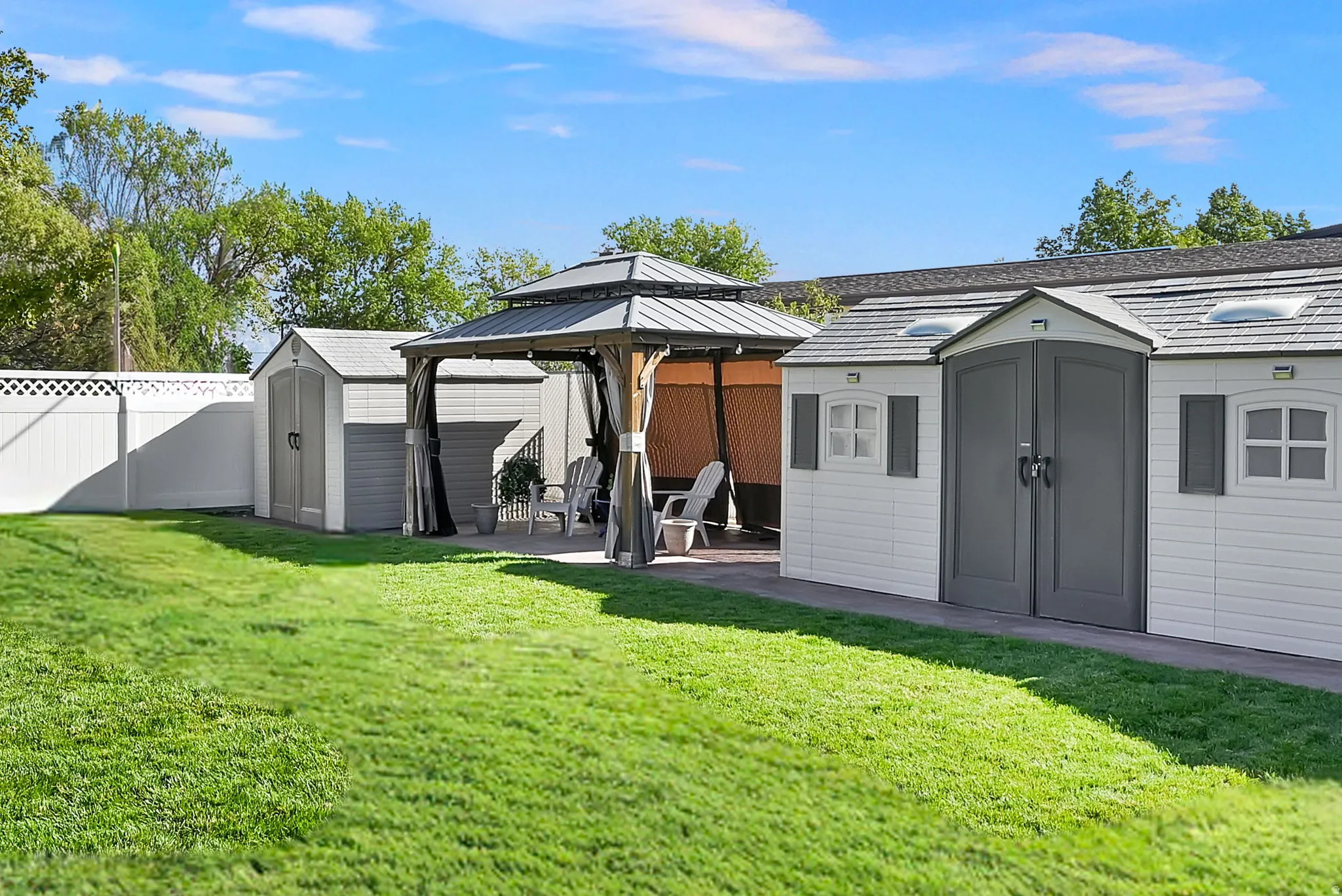Expansive backyard featuring a gazebo, three storage sheds, and a white vinyl privacy fence