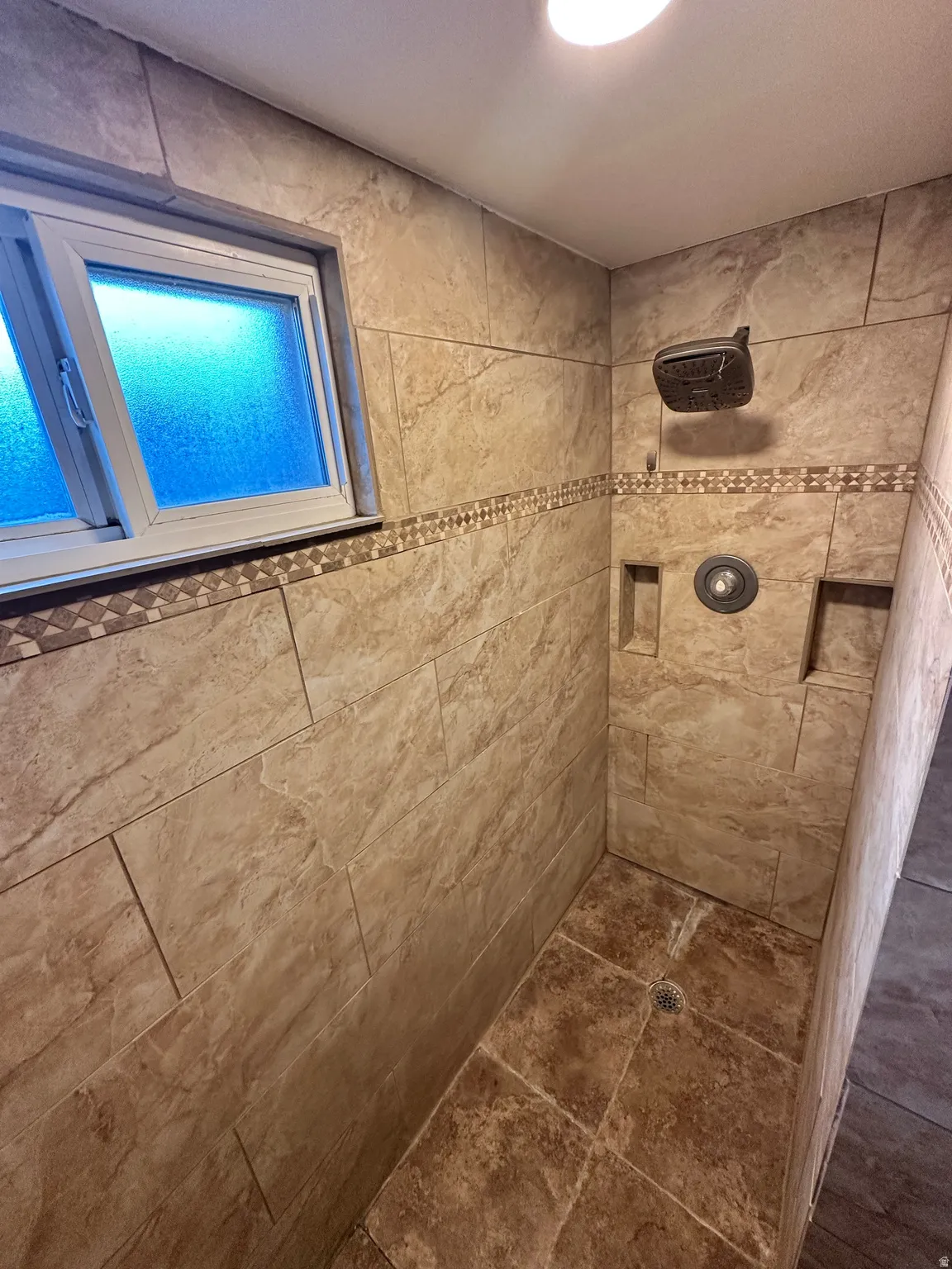 The tiled shower enclosure features a rainfall showerhead, a single-handle control, dual integrated niches, and a decorative tile border.