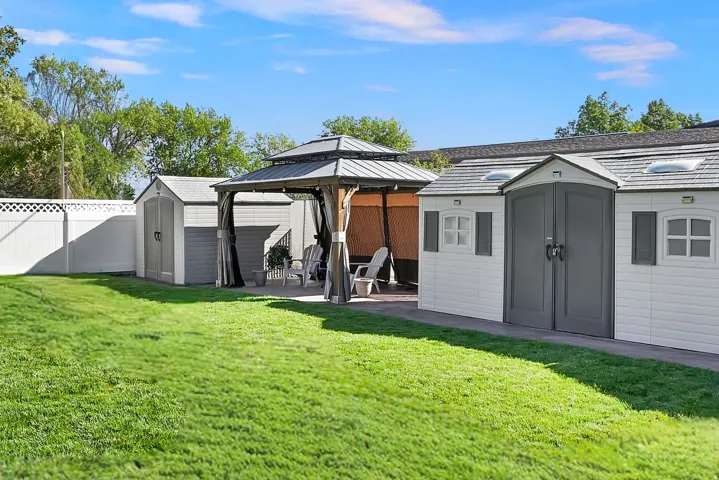 Expansive backyard featuring a gazebo, three storage sheds, and a white vinyl privacy fence