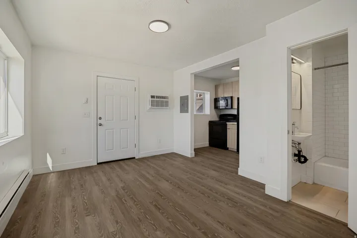 Wood-finish flooring throughout, bright white walls, and an included window air conditioning unit