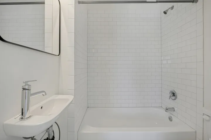 Integrated shower and bathtub with white subway tile surround, chrome fixtures, and a wall-mounted sink with a modern faucet