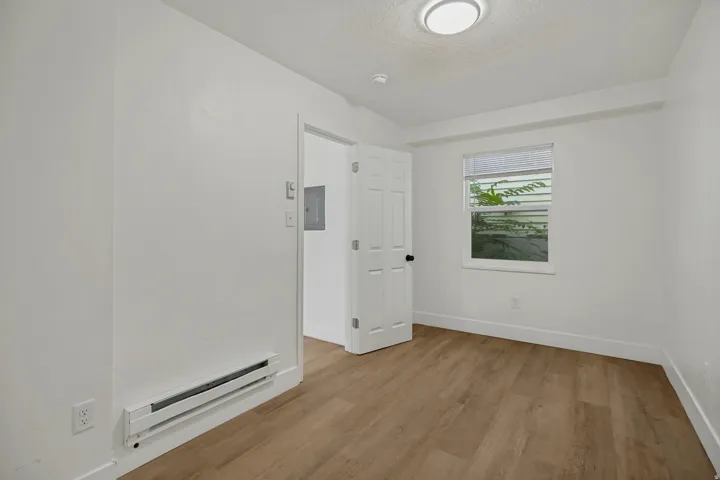 Bright, light-filled bedroom featuring wood-finish flooring, recessed ceiling lighting, and large window with natural light
