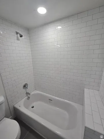 Bathtub with subway tile surround, chrome fixtures, and built-in tiled bench