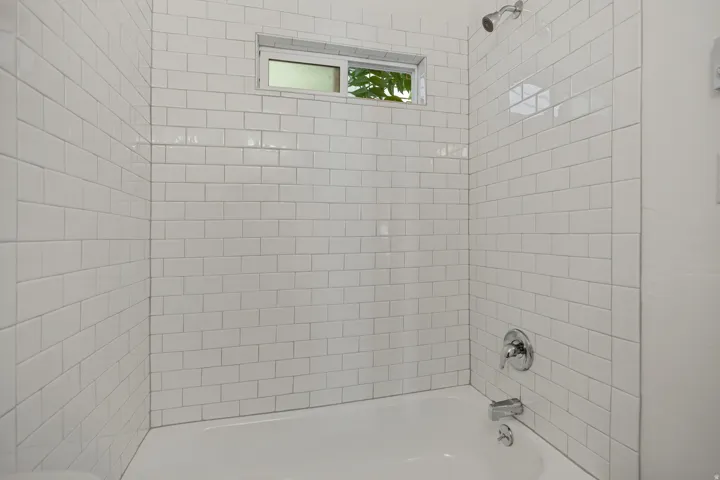 Bathtub with white subway tile surround, chrome showerhead, and integrated window