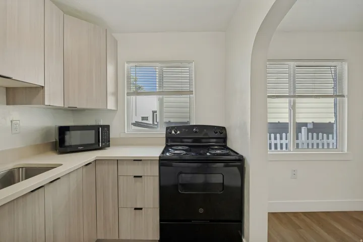 Contemporary kitchen featuring light wood-finish cabinetry, light-toned countertops, a stainless steel sink, and a black range