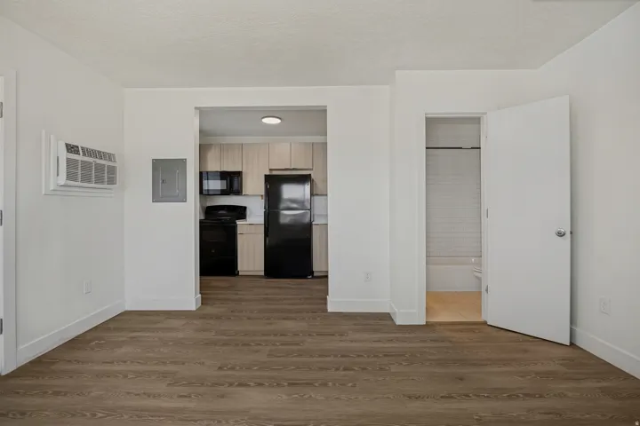 Wood-finish flooring throughout, with a kitchen featuring light wood-tone cabinetry, dark appliances, and a white countertop
