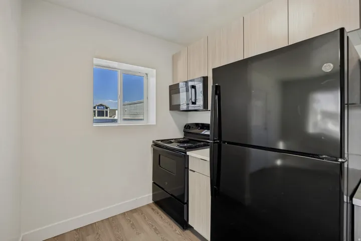 Kitchen featuring wood-finish flooring, light-toned upper cabinetry, black refrigerator, black range, and an over-the-range microwave