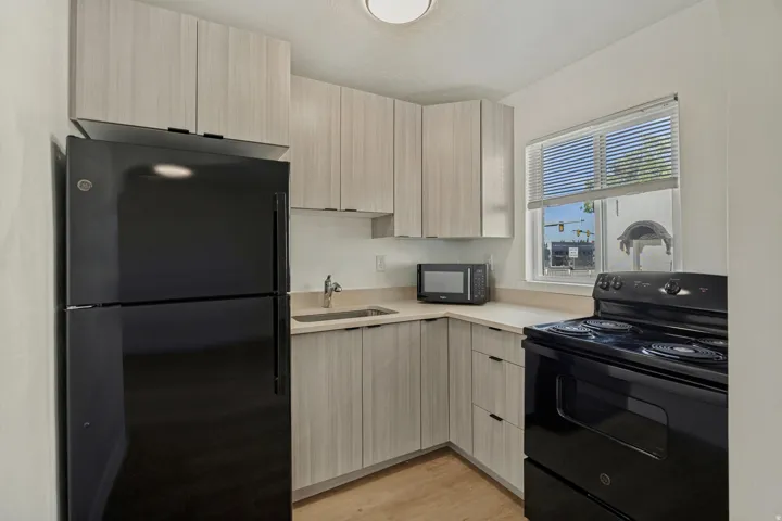 White cabinetry, white countertops, black refrigerator, black range, and wood-finish flooring