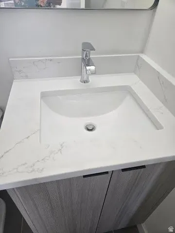 Integrated vanity sink with a polished chrome faucet, set into a stone-finish countertop with a matching backsplash, above wood-finish cabinetry