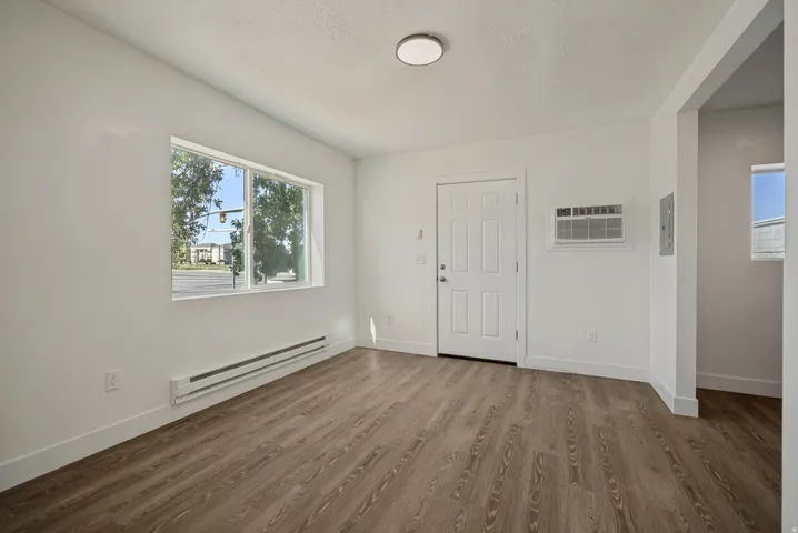 Wood-finish flooring, white paneled entry door, window with exterior scenery, wall-mounted air conditioning unit, and flush-mount ceiling light fixture