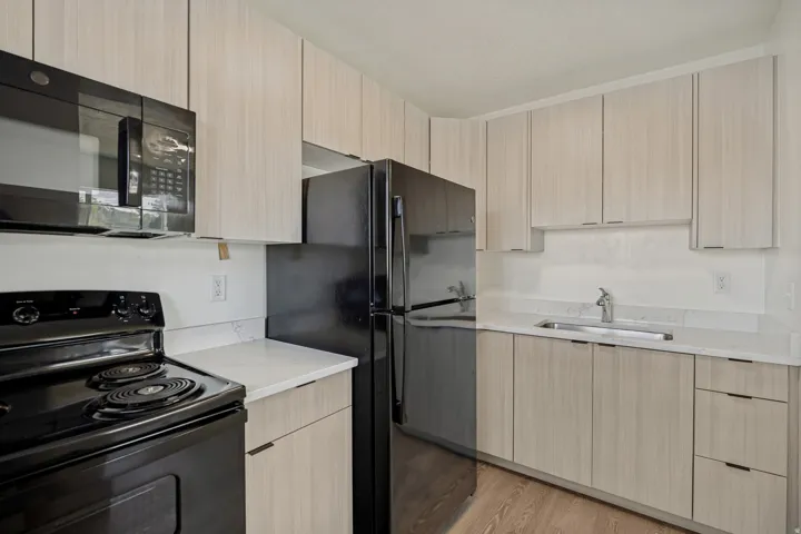 Kitchen featuring light wood-finish cabinetry, black appliances, white countertops, and a stainless steel sink