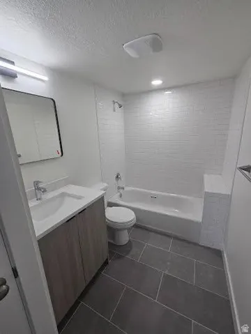 Vanity with integrated sink, wood-finish cabinetry, subway tile shower surround, bathtub, and large format floor tiling