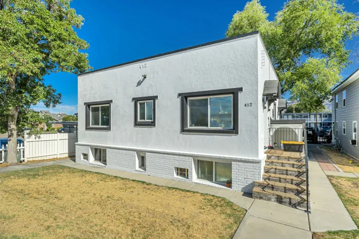 Stucco exterior with black trim windows, white picket fence, and a stone-finish staircase with metal railings