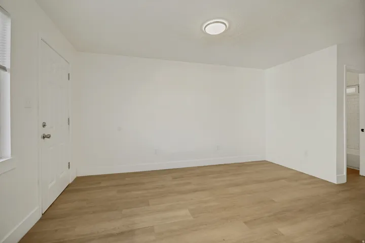 Wood-finish flooring, white walls, flush-mount ceiling light, paneled door, and window with blinds
