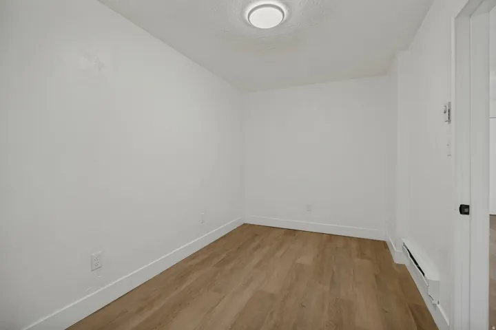 Bright, clean bedroom with wood-finish flooring, white walls, and recessed ceiling lighting