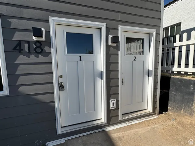 Gray horizontal siding, two white entry doors with window panes, and wall-mounted exterior light fixtures