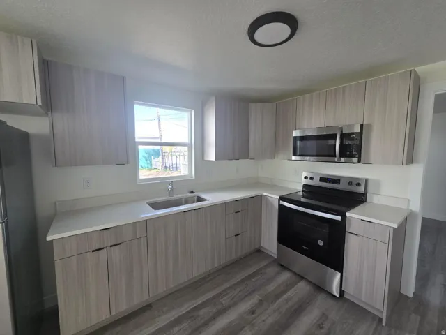 Modern kitchen featuring light wood-finish cabinetry, stainless steel appliances including a slide-in electric range and microwave, laminate countertops with an undermount sink, and wood-finish plank flooring throughout