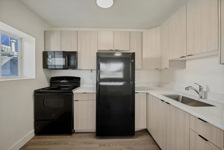 Kitchen featuring light wood-finish cabinetry, white countertops, a black range, an over-the-range microwave, and a black refrigerator