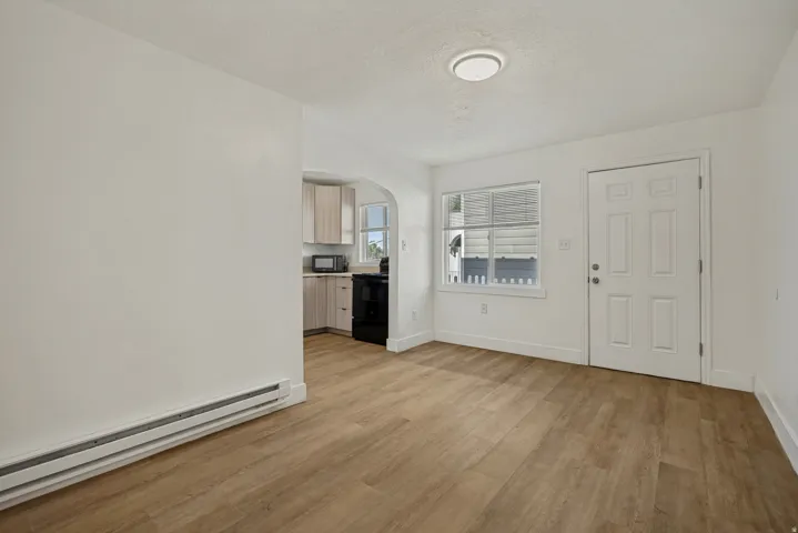 Wood-finish flooring throughout, white paneled door, flush-mount ceiling lighting, arched entryway, and light-toned cabinetry