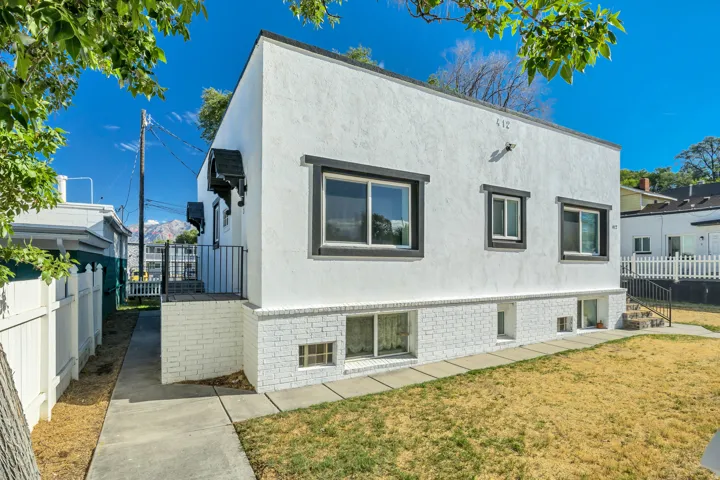 White stucco exterior with dark trim windows, white painted brick foundation, and a concrete walkway