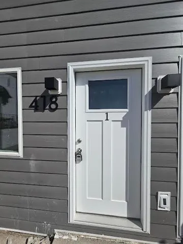 White entry door with a top light, dark gray horizontal siding, and black exterior lighting fixtures