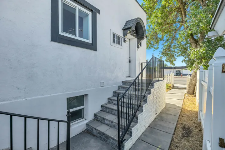 Stucco exterior with contrasting trim, stone-finish steps with metal railings, and a side walkway leading to a white picket fence