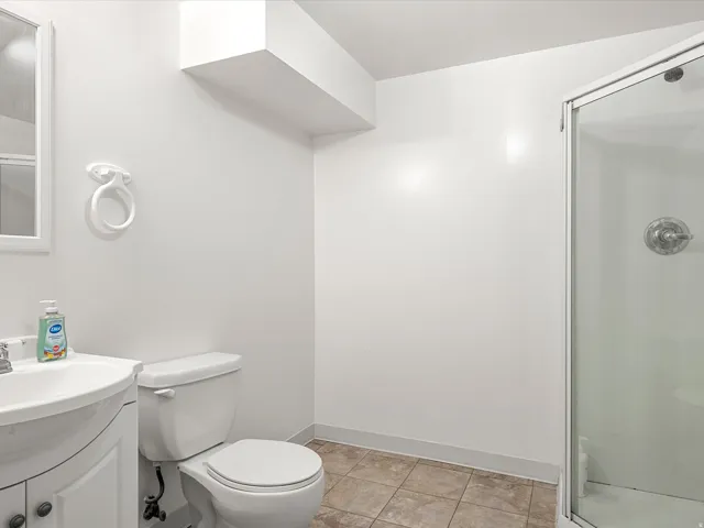 White vanity with integrated sink, chrome faucet, toilet, glass-enclosed shower, and tiled flooring