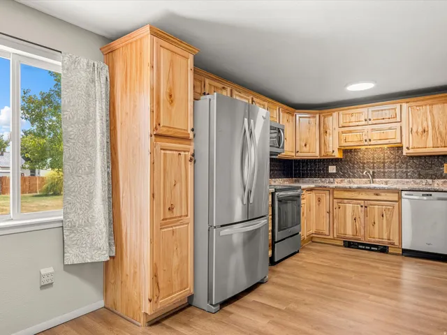 Kitchen featuring wood-finish cabinetry, stainless steel appliances, patterned backsplash, and wood-finish flooring
