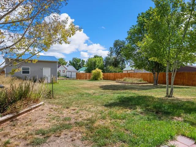 Expansive backyard featuring a partial wood fence, mature trees, and raised garden beds