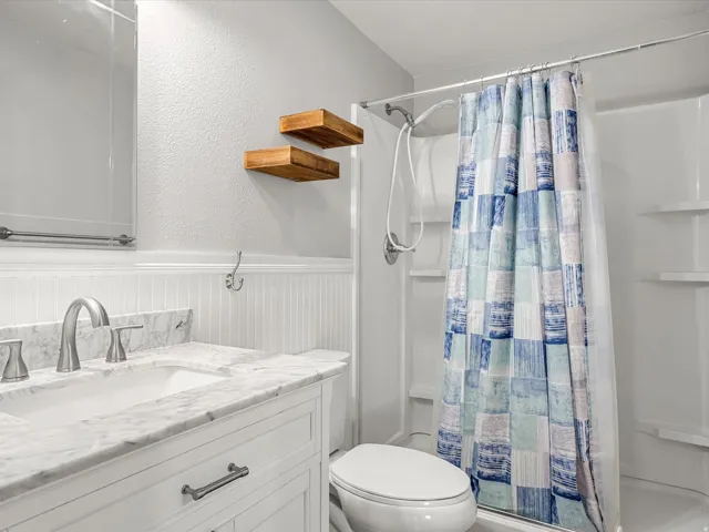 White vanity with a light-toned countertop, beadboard wainscoting, and a white shower stall with built-in shelving