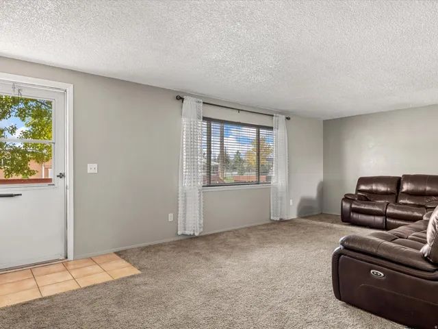 Carpeted living space with a window featuring horizontal blinds, a white entry door, and a tiled entry area
