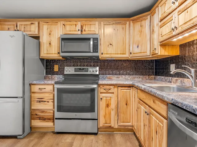 Kitchen featuring wood cabinetry, stainless steel appliances, dark embossed backsplash, and a double basin sink