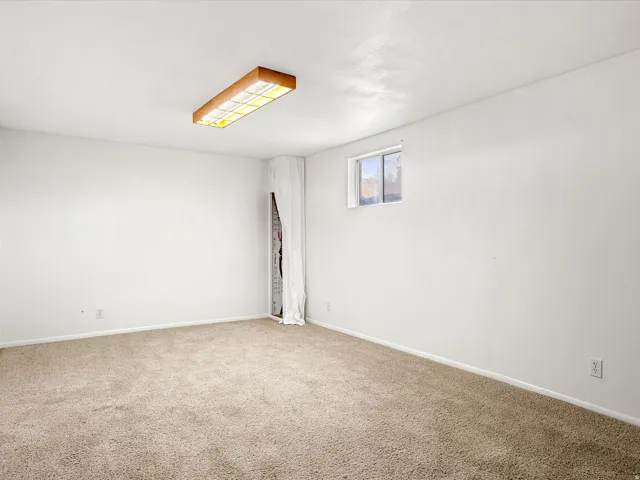 Spacious carpeted room with neutral wall finishes, recessed ceiling lighting, and a single window providing natural light