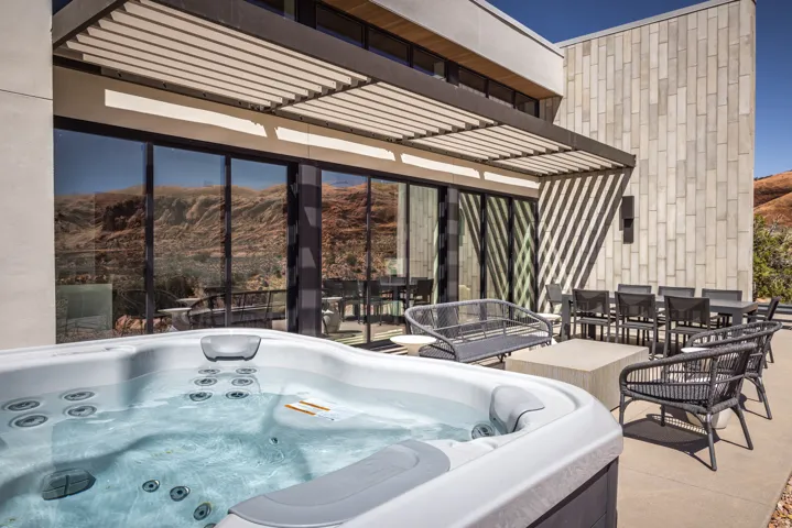 Outdoor spa with a concrete patio featuring a dining area, a slatted pergola, and a stone-clad exterior wall