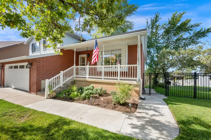 Brick exterior with white siding accents, covered front porch, attached two-car garage, established landscaping, and black wrought iron fencing