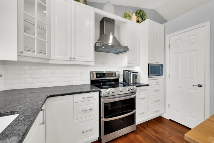 White shaker cabinetry, black speckled countertops, stainless steel appliances, white subway tile backsplash, and wood-finish flooring