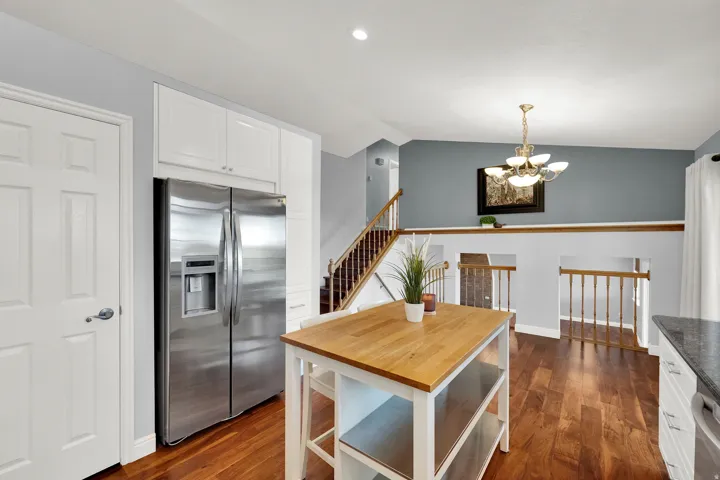 Hardwood flooring, white cabinetry, stainless steel refrigerator, white paneled door, and built-in kitchen island