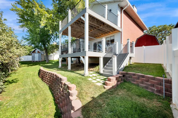 Two-story deck with metal railings and staircase, tiered landscaping with retaining walls, fenced yard, and exterior storage shed